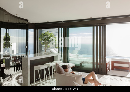 Frau im modernen Wohnzimmer mit Blick auf Meer Stockfoto