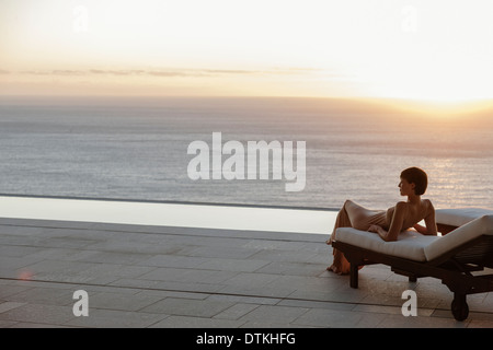 Frau im Kleid, die Verlegung auf Liegestuhl auf der Terrasse mit Blick auf Meer bei Sonnenuntergang Stockfoto