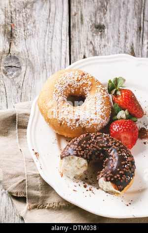 Zucker und die Hälfte der Schokoladen Donuts und frische Erdbeeren auf weißem Teller auf Holztisch serviert. Serien ansehen Stockfoto