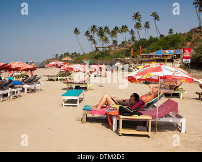 Indien, Goa, große Vagator Strand, russische Touristen auf Sonnenliegen am Balken unter hohen Kokospalmen Stockfoto