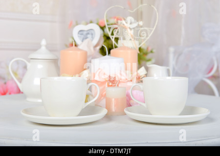 Kaffeetassen und Kerzen auf einem weißen Tisch. Romantisches Abendessen. Stockfoto