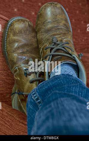 Altes Paar Schuhe im Ruhestand als Hausschuhe auf dem Sofa am Ende auf Jean gekleidete Beine: Entspannung Stockfoto