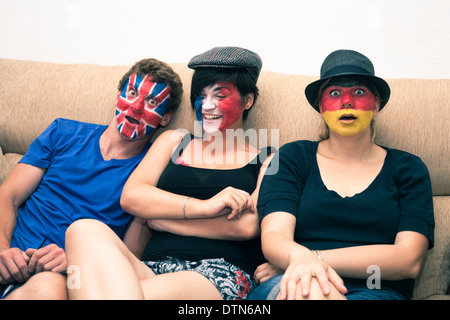 Gruppe von lustigen Menschen mit bemalten Fahnen auf ihren Gesichtern und sitzt auf dem Sofa. Stockfoto
