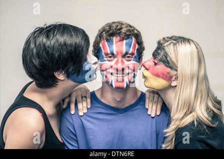 Glückliche Frauen küssen Mann mit bemalten europäischen Flaggen auf ihren Gesichtern. Stockfoto