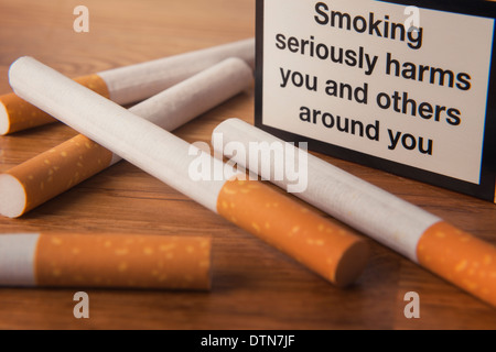Einige Zigaretten und ein Paket mit Warnhinweis auf einer Oberfläche. Stockfoto