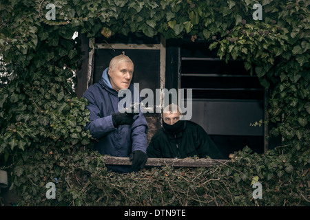 Zwei maskierte bewaffnete Männer verstecken auf bewachsenen Veranda der alten Kabine. Stockfoto