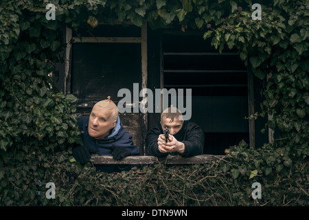 Zwei maskierte bewaffnete Männer verstecken auf bewachsenen Veranda der alten Kabine. Stockfoto