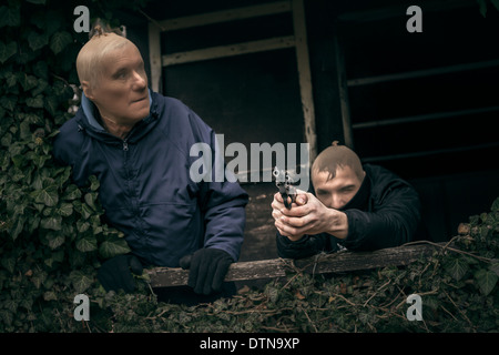 Zwei maskierte bewaffnete Männer verstecken auf bewachsenen Veranda der alten Kabine. Stockfoto