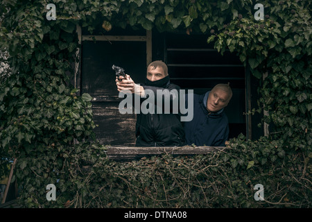 Zwei maskierte bewaffnete Männer verstecken auf bewachsenen Veranda der alten Kabine. Stockfoto