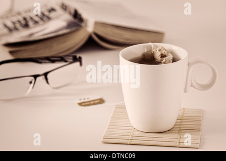 Tasse Tee mit Lesebrille und Buch Stockfoto