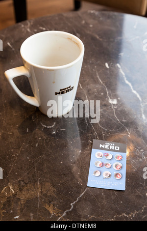 Vollständig ausgefülltes Caffe Nero-Kundenkarte mit allen Stempeln ausgefüllt neben leere Tasse Kaffee Stockfoto