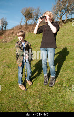 Zwei Jungs im Teenageralter in einem Feld stehen, sucht man durch ein Fernglas und die andere hält einen Spazierstock Stockfoto