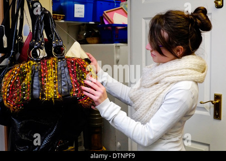 junge Frau in einem Charity-Shop Handtaschen zu betrachten Stockfoto