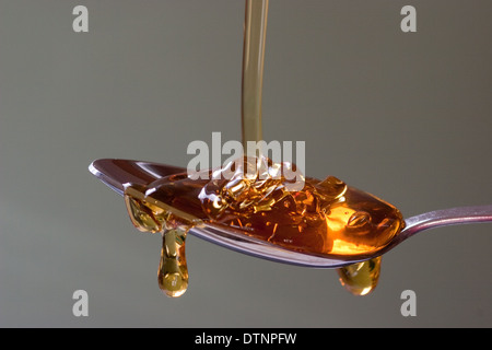 Goldener Sirup wird von oben auf einen Silberlöffel mit neutralem, glattem Hintergrund gegossen Stockfoto