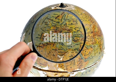 Hand hält eine Lupe über eine alte rotierenden Globus isoliert auf weißem Hintergrund Stockfoto