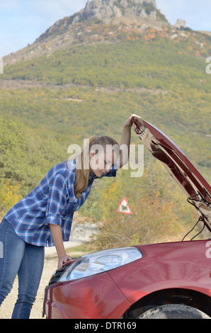 Junge Frau in der Nähe von kaputten Auto braucht Hilfe suchen unter geöffneter Haube Stockfoto