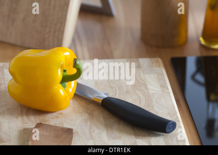 Gelbe Paprika liegt im rechten Bereich des Bildes mit einem Küchenmesser auf ein Schneidebrett mit Textfreiraum Stockfoto