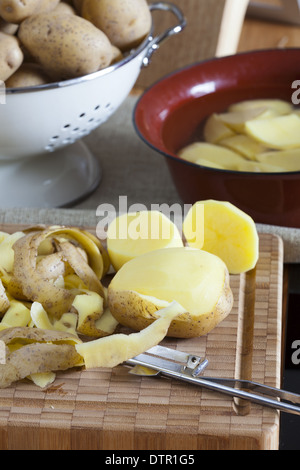 Rohe Kartoffeln und Sparschäler auf ein Schneidebrett Stockfoto