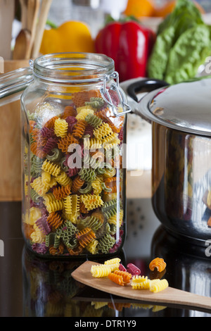 Großer Speicher Jar mit bunten Nudeln und Kochen Löffel mit textfreiraum im oberen und rechten Bereich des Bildes Stockfoto