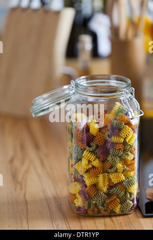 Lagerung Jar mit bunten Nudeln und Kochen Löffel auf Arbeitsplatte mit textfreiraum im linken und oberen Bereich des Bildes Stockfoto