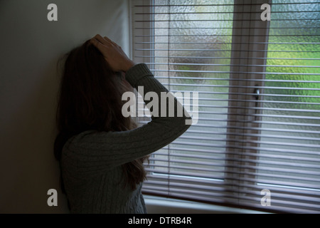 Nicht erkennbare junge Frau mit den Händen auf dem Kopf durch ein Fenster. Stockfoto