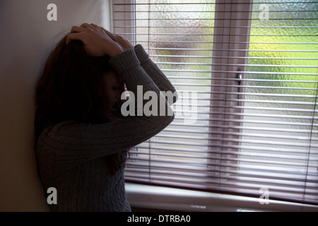 Nicht erkennbare junge Frau mit den Händen auf dem Kopf durch ein Fenster. Stockfoto