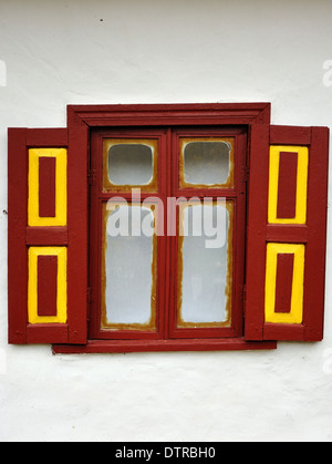 Öffnen Sie Fenster mit roten und gelben Fensterläden aus Holz in die weiße Wand Stockfoto