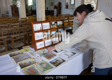 Ehrlichkeit-Box einkaufen: eine Frau Surfen unbeaufsichtigt Postkarten und andere Souvenirs zum Verkauf in St. Marys Kirche, Kersey, England. Stockfoto