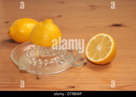 halben Zitrone gequetscht auf ein Glas Saftpresse/Entsafter mit eineinhalb Zitronen im Hintergrund auf Kiefer (2 Reihe von 4) Stockfoto