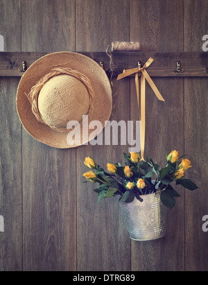 Rustikale Scheune Tür mit hängenden Strohhut und Eimer mit gelben Rosen Stockfoto