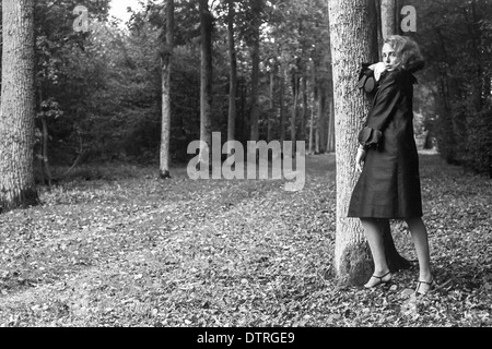 60er Jahre Mode Modell mit schwarzen Mantel posiert im Wald Stockfoto