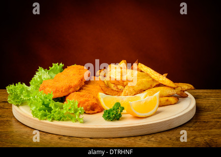 Stillleben mit traditionellen Fisch und Chips, Zitronen, auf einer Holzplatte Stockfoto