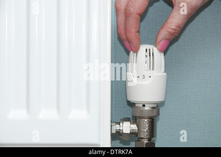 Frau drehen thermostatischen/Heizkörper/Ventil nach oben/unten auf Zentralheizung im heimischen Zuhause, England, UK Stockfoto