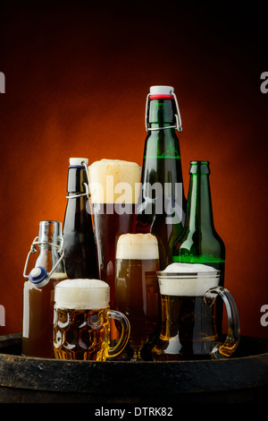 Stilleben mit verschiedenen Bierflaschen und Gläser auf einem Holzfass Stockfoto