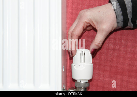 Frau drehen thermostatischen/Heizkörper/Ventil nach oben/unten auf Zentralheizung im heimischen Zuhause, England, UK Stockfoto