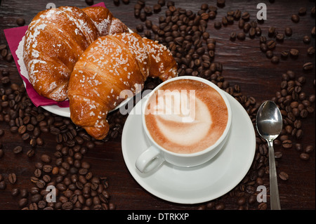 Cappuccino und Croissant mit Kaffeebohnen Stockfoto