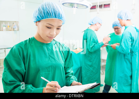 Frau Chirurgen schreiben Krankenakte mit Teams im OP-Saal Stockfoto