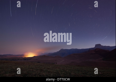 Sternspuren über ein Buschfeuer unter dem Amphitheater-Bereich in den Drakensbergen, Südafrika Stockfoto