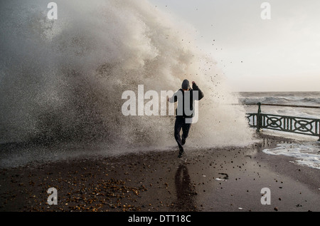 Ein Mann läuft von riesigen Wellen während der Gezeiten Überspannungen auf britischen Küsten bei extremem Wetter. Szene in Brighton, Sussex, Großbritannien Stockfoto