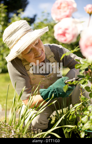 Beautiful senior Woman schneiden Blumen Pflanzen in ihrem Garten lächelnd - Seniorin im Garten im Hinterhof