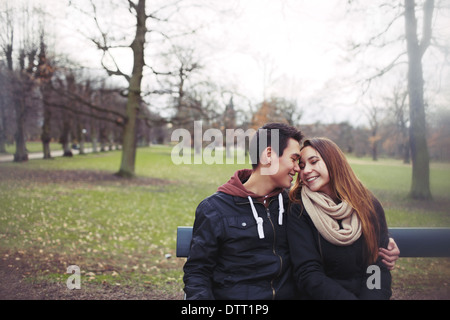 Romantische junges Paar sitzt auf einer Parkbank im Freien im Winter. Gemischte Rassen Teenager-Paar zusammen in romantischen Moment. Stockfoto