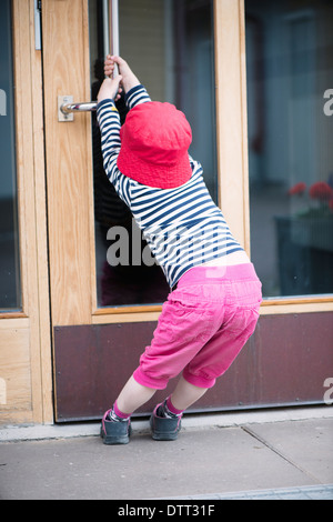 Junges Kind kämpfen mit schweren Tür öffnen durch Ziehen am Griff Stockfoto