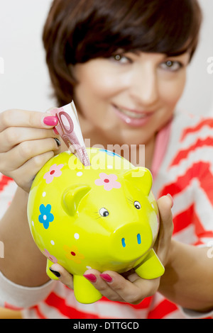 Kaukasische Mädchen gibt Geld für dekorative Keramik Sparschwein. Stockfoto