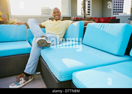 Schwarzer Mann auf Sofa auf städtischen Balkon entspannen Stockfoto