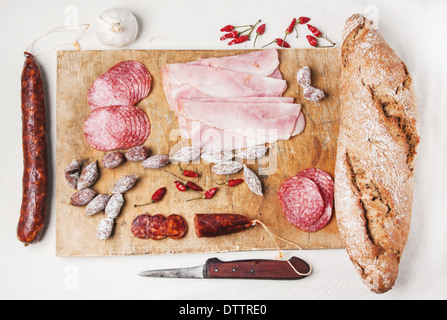 Draufsicht auf Holzbrett mit Schinken und Salami Wurst mit frischem Brot und Chilischoten mit Vintage Messer serviert. Stockfoto