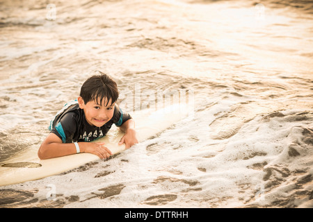 Hispanische junge schwimmt auf Surfbrett im Ozean Stockfoto