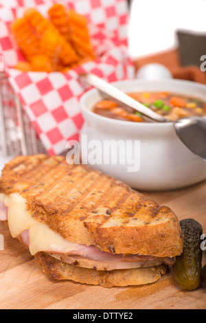 Leckeres Panini mit Schinken, Schweinefleisch und Schweizer Käse, serviert mit einem Gemüse Suppe, Pickles und Süßkartoffel Pommes frites gemacht Stockfoto