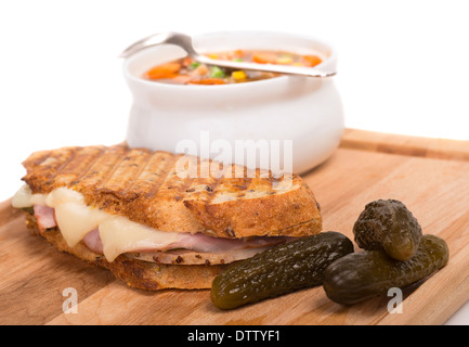 Leckeres Panini mit Schinken, Schweinefleisch und Schweizer Käse, serviert mit einer Gemüsesuppe und Gurken gemacht Stockfoto