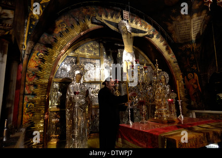 Ein griechisch-orthodoxer Kleriker zündet Kerzen am Altar der Kreuzigung im Golgatha an, der traditionell als Ort der Kreuzigung Jesu angesehen wird. Der Hauptaltar gehört zu den griechisch-orthodoxen, die den Felsen von Golgatha 12. Station des Kreuzes in der Kirche des Heiligen Grabes enthält Alte Stadt Ost-Jerusalem Israel Stockfoto