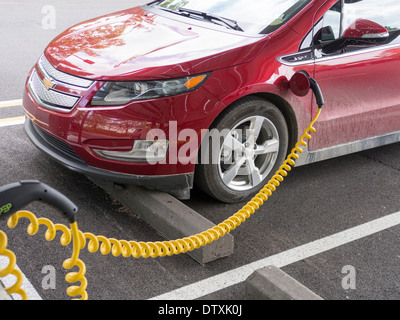 Ein Elektroauto aufladen. Ein Plug-in-Chevrolet Volt Auto an einem Parkplatz Ladestation angeschlossen. Stockfoto